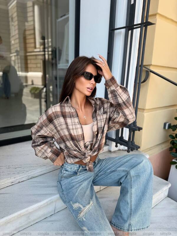 Woman sitting on a bench wearing a plaid shirt and jeans, with a building in the background.