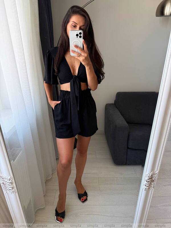 Person taking a mirror selfie wearing a black outfit in a room with a gray sofa.