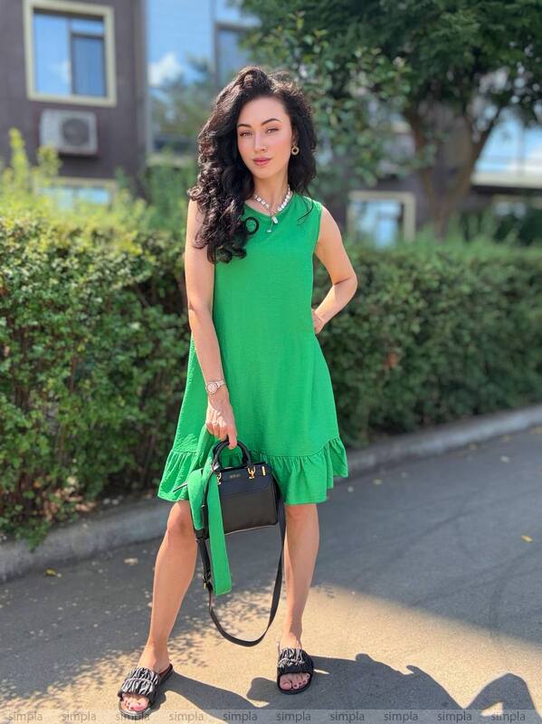 Woman in a green dress standing outdoors with bushes and a building in the background