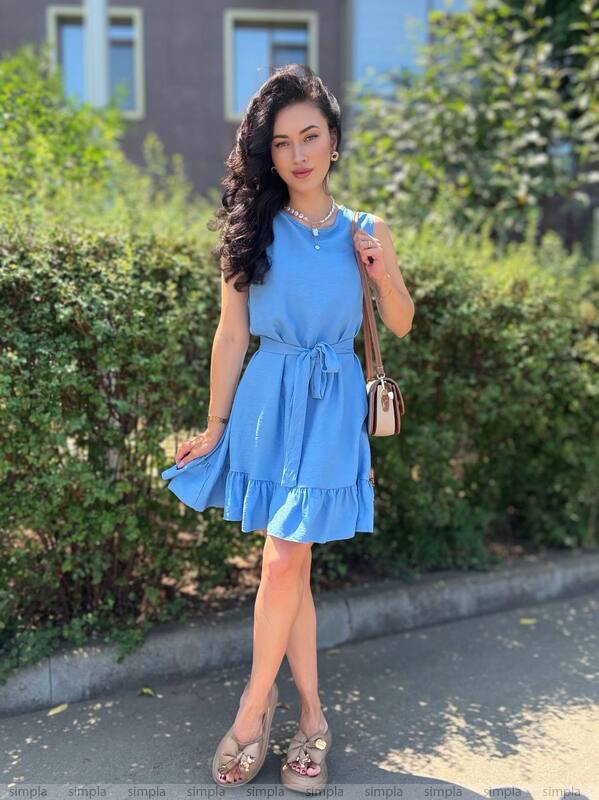 Woman in a blue dress standing outdoors with greenery in the background