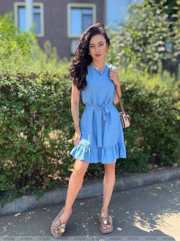 Woman in a blue dress standing outdoors with greenery in the background