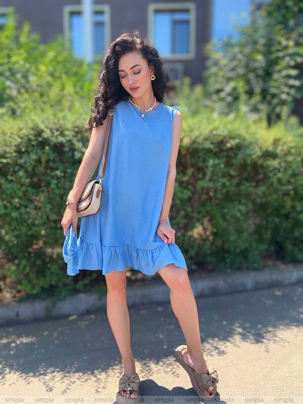 Woman wearing a blue dress standing outdoors with greenery in the background