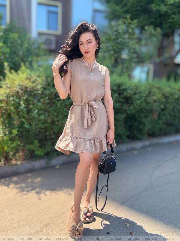 Woman in a beige dress standing outdoors with greenery in the background