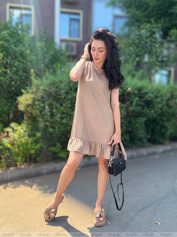 Woman in a beige dress standing outdoors with greenery in the background