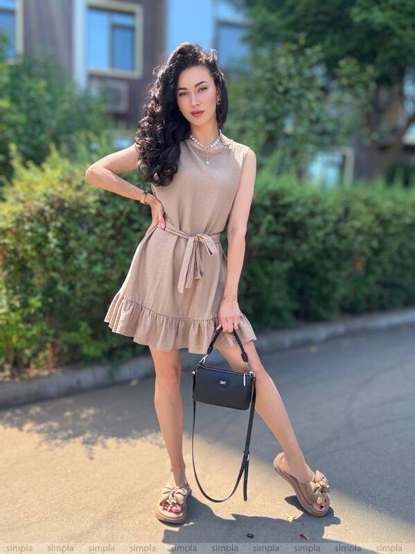 Woman in a beige dress standing outdoors with greenery in the background
