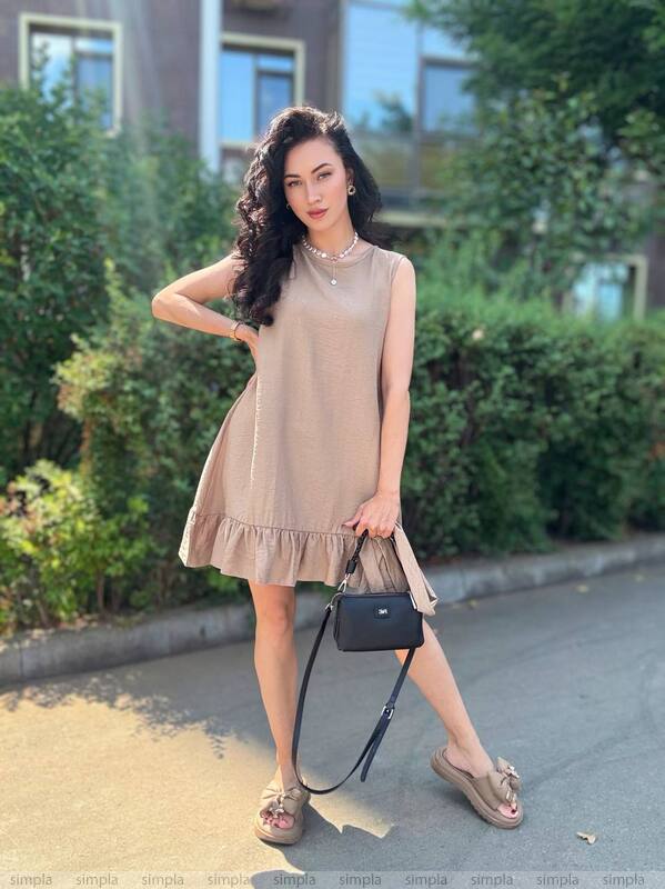 Woman in a beige dress standing outdoors with greenery in the background