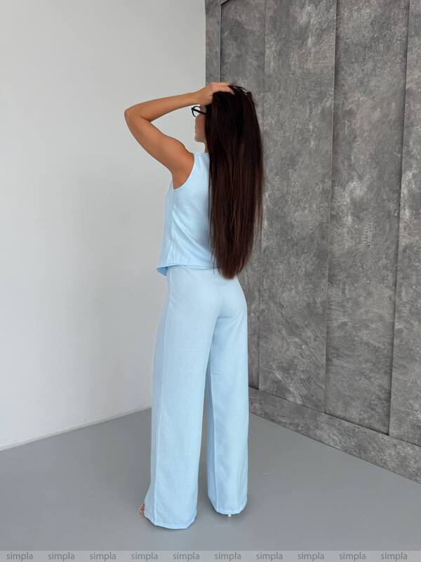 Woman in light blue outfit standing against a gray wall.