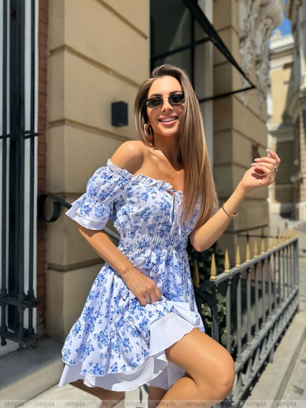 Woman in a blue floral dress standing outdoors with buildings in the background