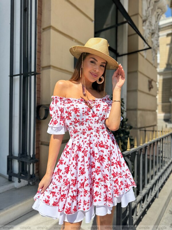 Woman wearing a red floral dress and beige hat on a city street.