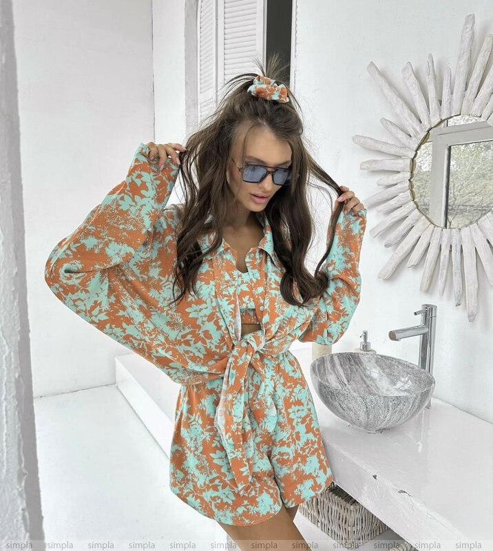 Woman in a floral dress standing in a bathroom with a mirror and sink.