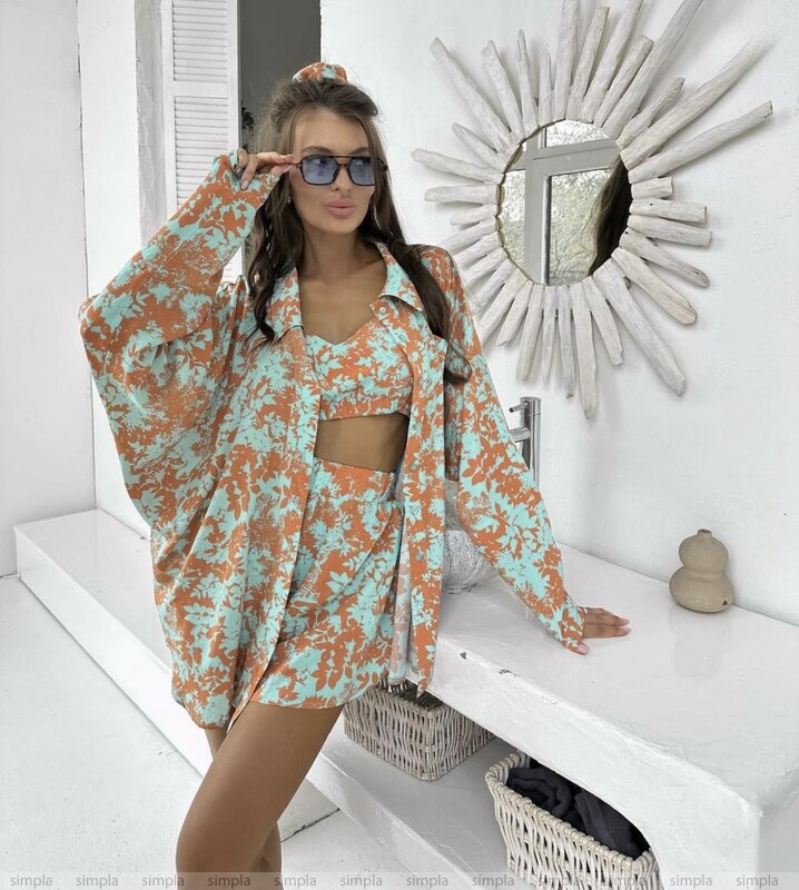 Woman in a floral outfit standing in a bright room with a decorative mirror.
