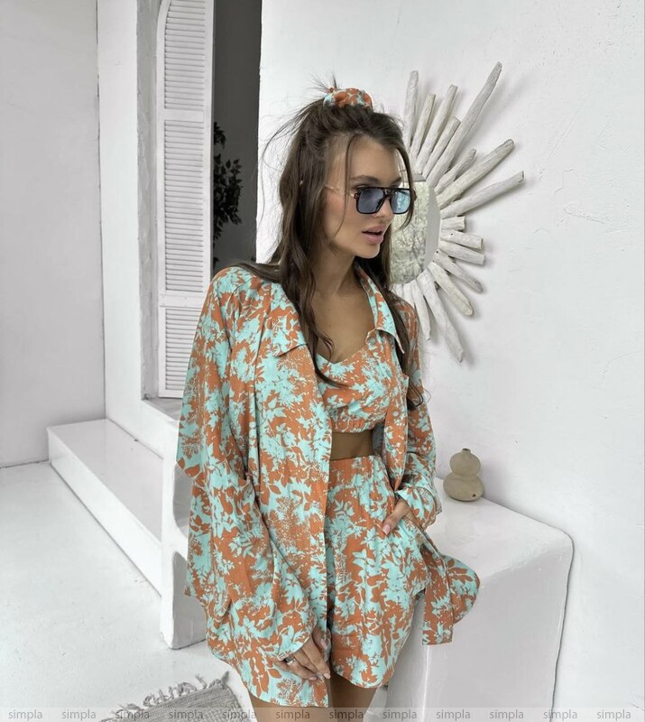 Woman in a floral outfit sitting on a white bench with a decorative wall mirror in the background.