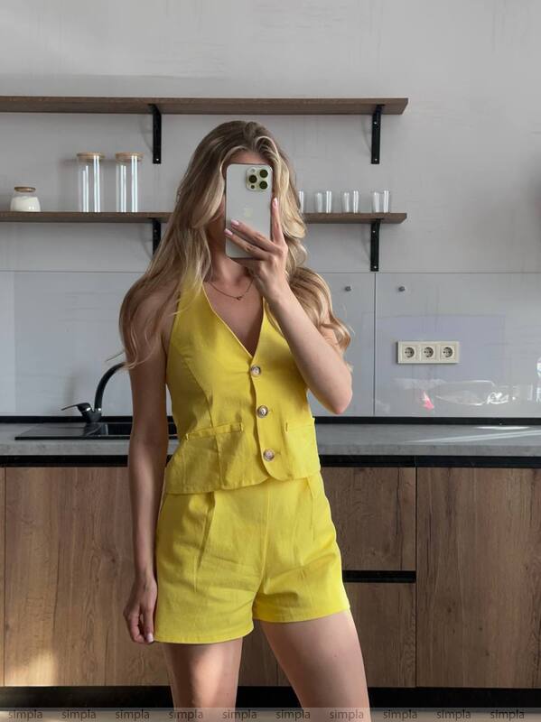 Woman in a yellow outfit taking a mirror selfie in a kitchen.