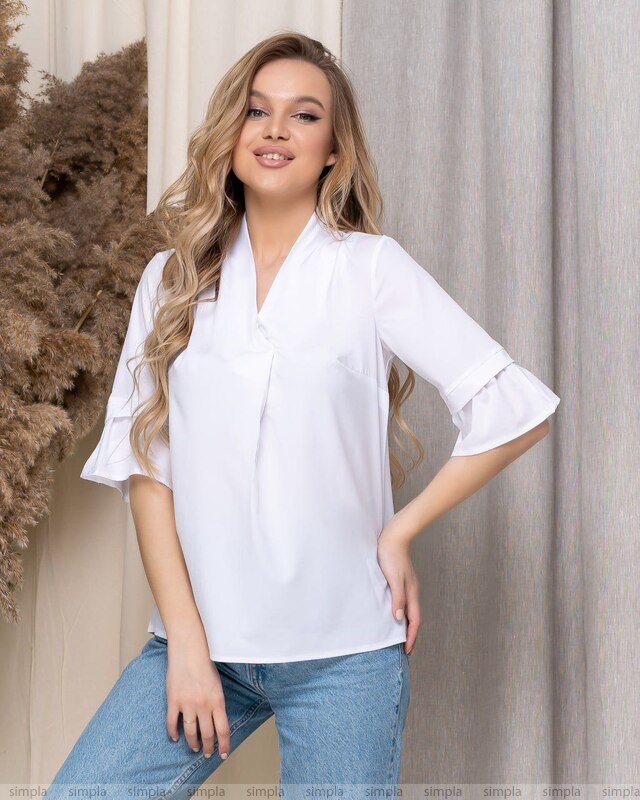 Woman wearing a white blouse and blue jeans standing against a neutral background