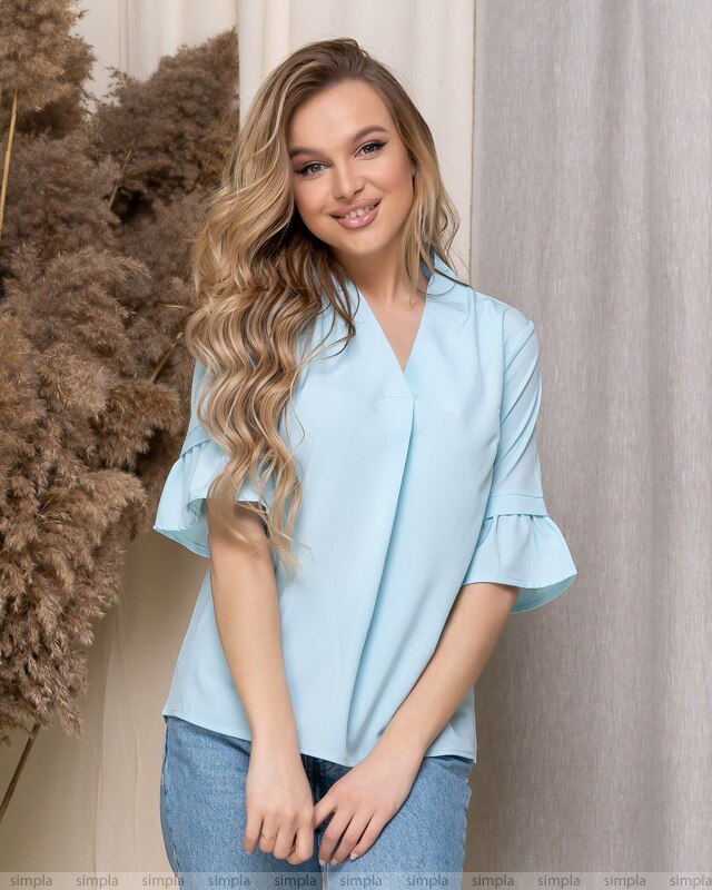 Woman wearing a light blue blouse with ruffled sleeves against a neutral background
