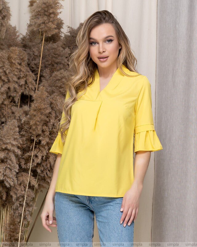 Woman wearing a yellow blouse with ruffled sleeves against a neutral background