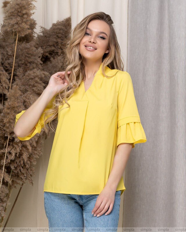 Woman wearing a yellow blouse with ruffled sleeves against a neutral background