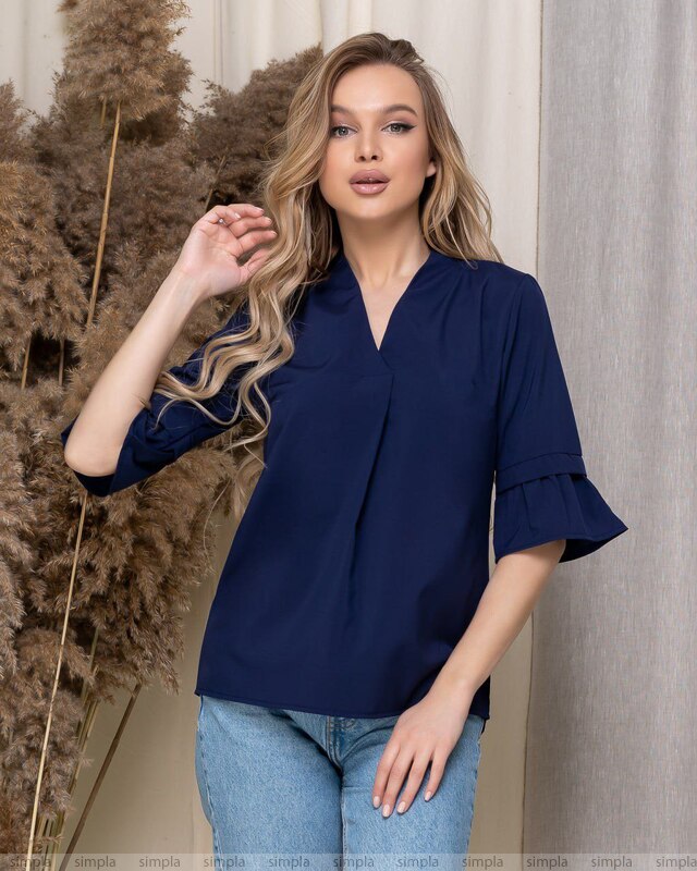 Woman wearing a navy blue blouse with ruffled sleeves against a neutral background