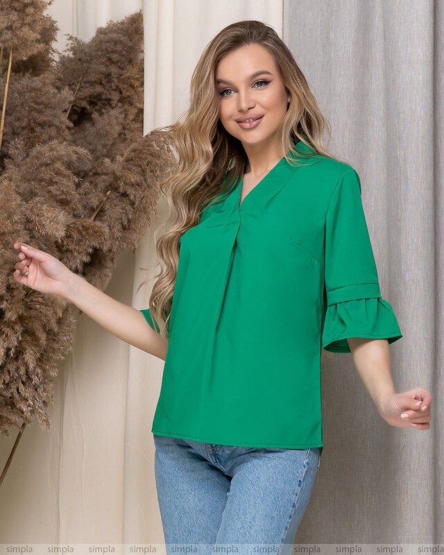 Woman wearing a green blouse with ruffled sleeves against a neutral background