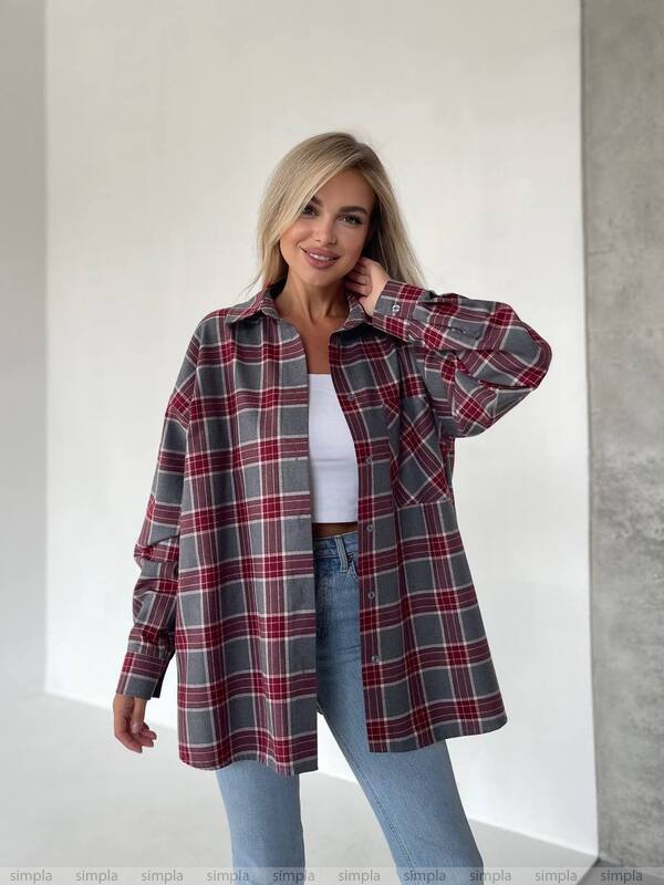 Woman wearing a plaid shirt over a white top and jeans against a plain background