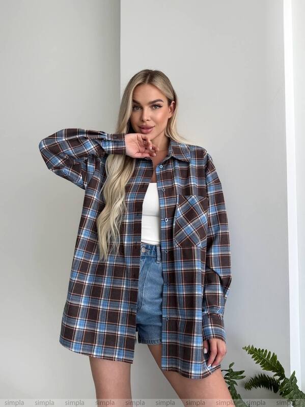 Woman wearing a plaid shirt over a white top and denim shorts against a plain background