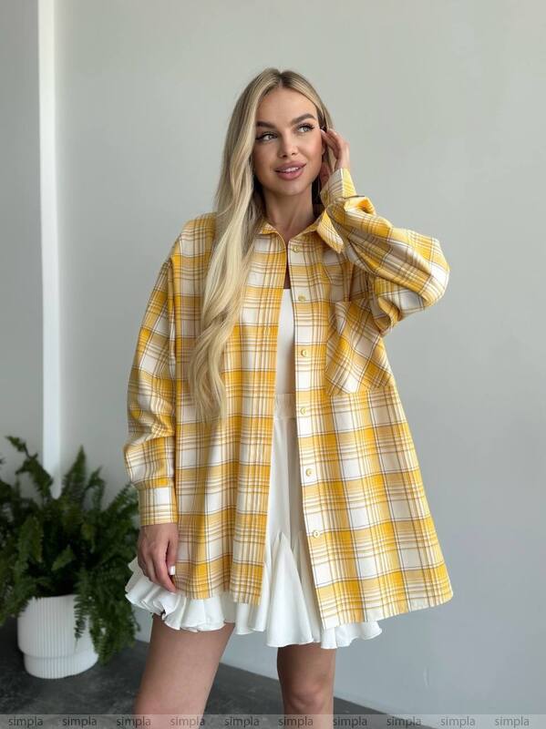 Woman wearing a yellow plaid shirt over a white dress against a neutral background