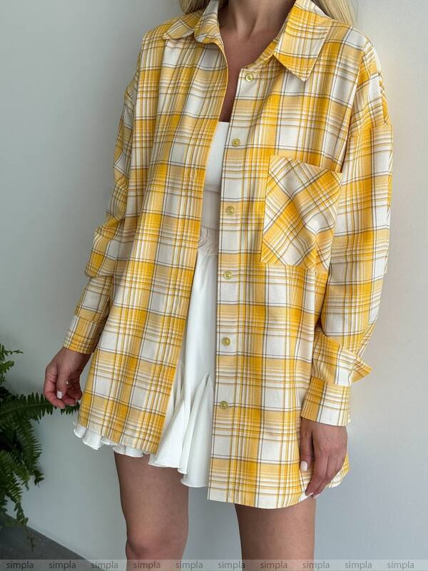 Person wearing a yellow and white plaid shirt over a white dress against a plain background