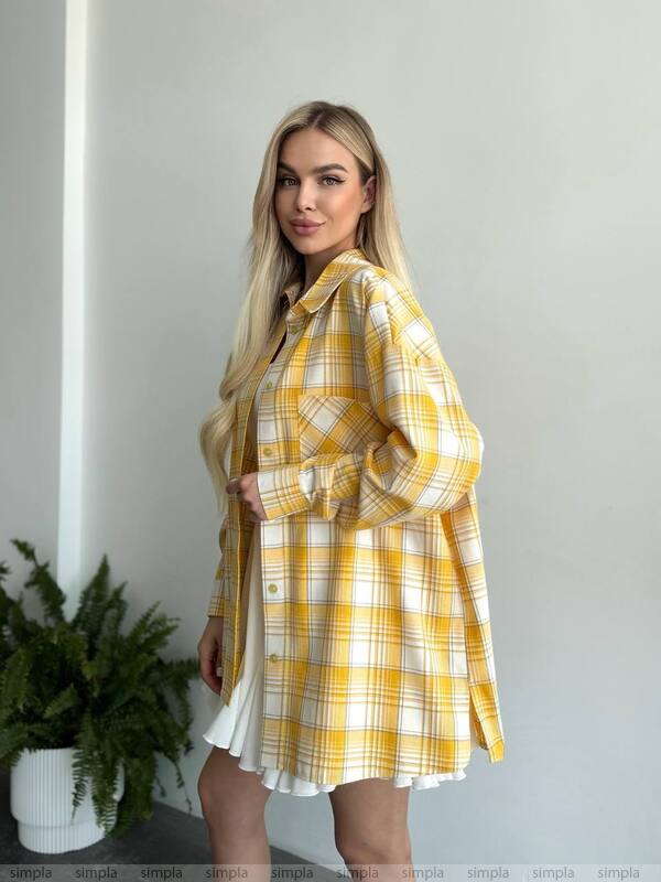 Woman wearing a yellow and white plaid shirt over a white dress, standing against a plain background.