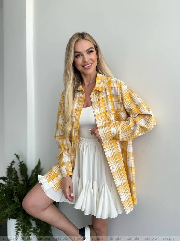 Woman wearing a yellow plaid shirt over a white dress against a plain background