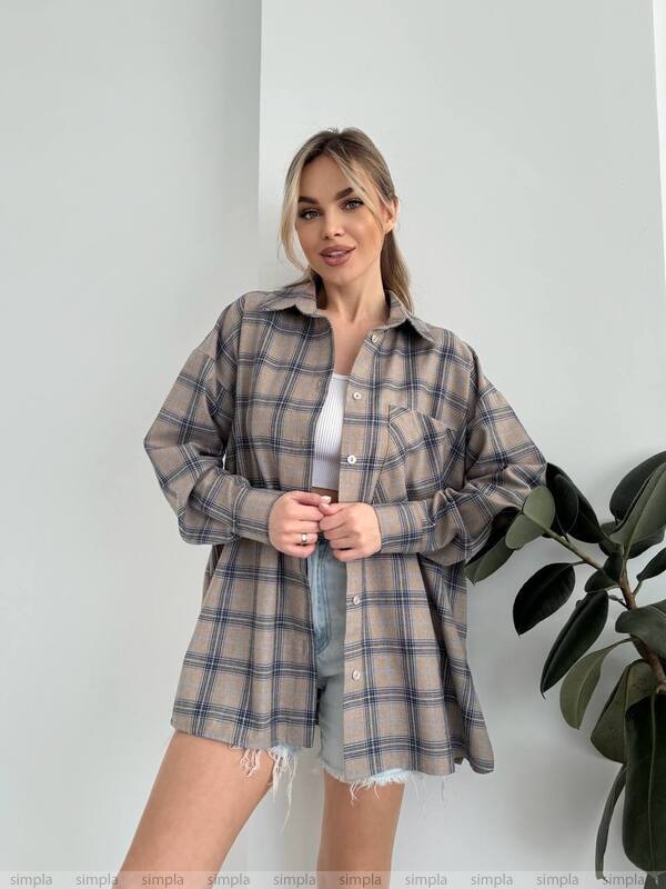 Woman wearing a plaid shirt over a white top with a plant in the background