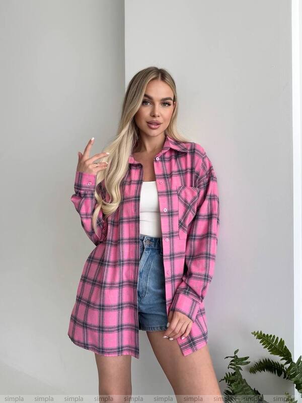 Woman wearing a pink plaid shirt over a white top and denim shorts against a plain background