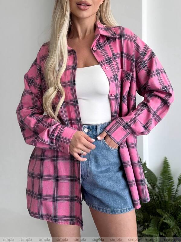 Woman wearing a pink plaid shirt over a white top and denim skirt on a plain background