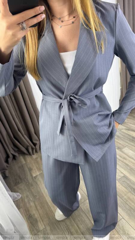 Person wearing a gray suit with a white top, standing indoors.