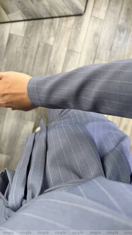 Gray pinstripe suit jacket being worn by a person against a wooden panel background