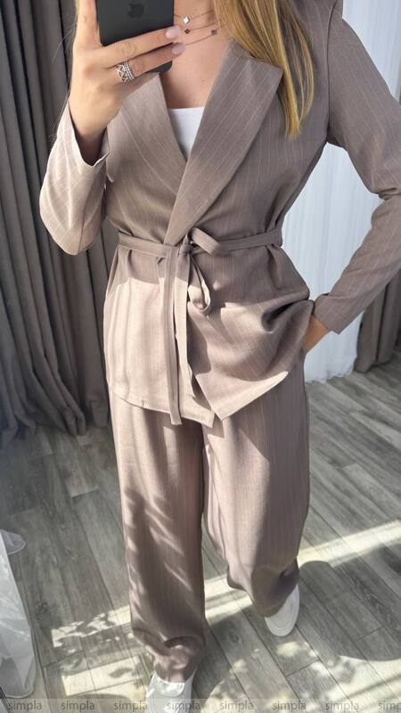 Person wearing a beige trench coat and pants in front of a mirror.