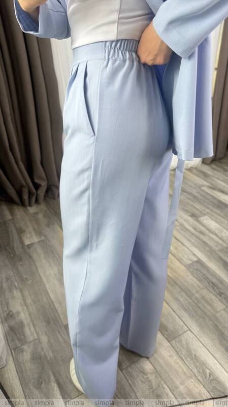 Person wearing a light gray outfit with wide-leg pants on a wooden floor.