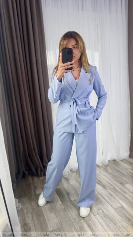 Woman wearing a light blue suit taking a mirror selfie.
