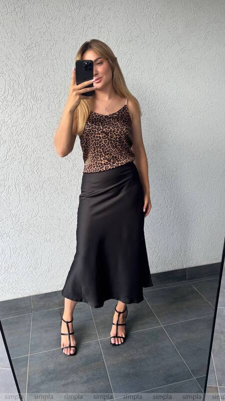 Woman taking a mirror selfie wearing a leopard print top and black skirt.