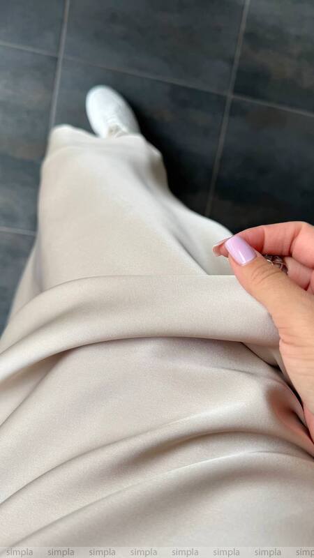 Close-up of beige pants with a hand touching the fabric on a dark tiled floor.