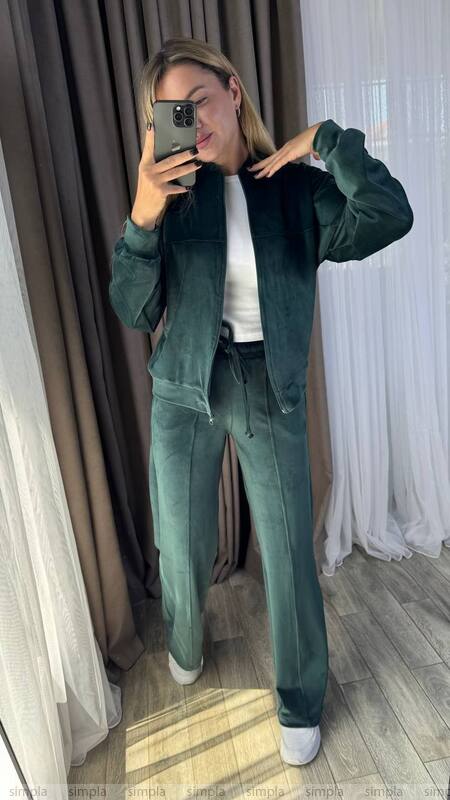 Person wearing a green tracksuit taking a mirror selfie indoors.