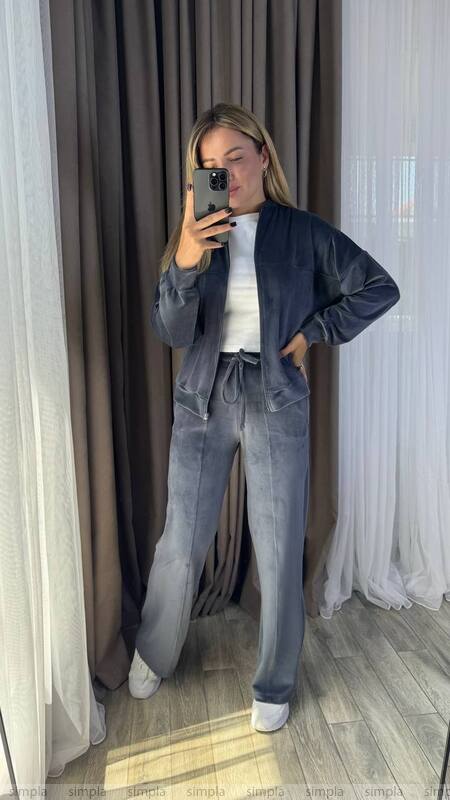 Person wearing a dark blue jacket and gray pants standing in front of a curtain.