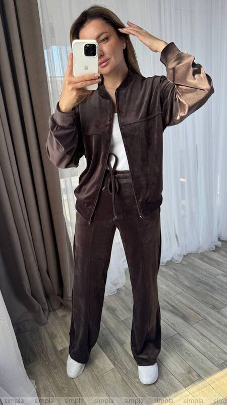 Woman taking a mirror selfie wearing a brown tracksuit in a room with curtains.