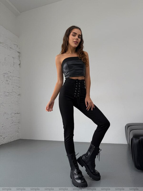 Woman wearing a black outfit with a strapless top and high-waisted pants in a minimalistic room.