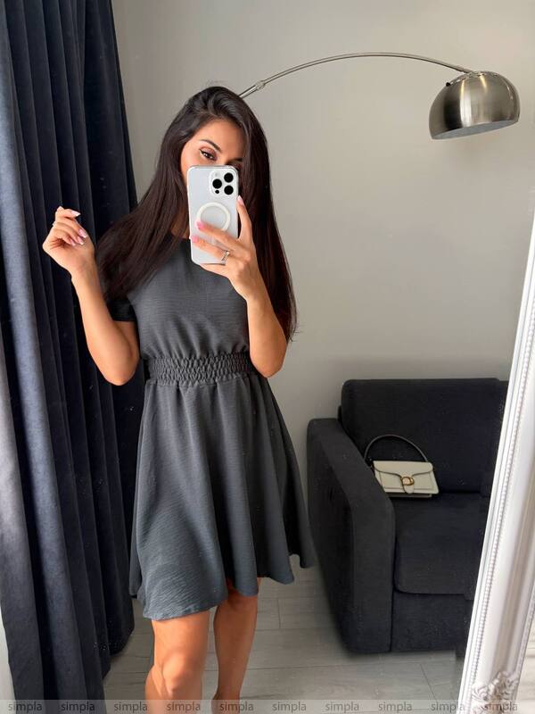 Woman taking a mirror selfie wearing a gray dress in a room with a lamp and couch.