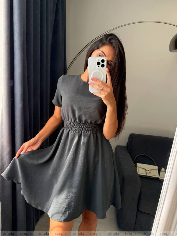 Woman taking a mirror selfie wearing a gray dress in a room with a couch and lamp.