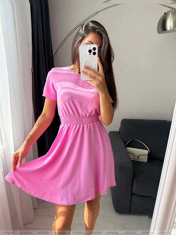 Person wearing a pink dress taking a mirror selfie in a room.