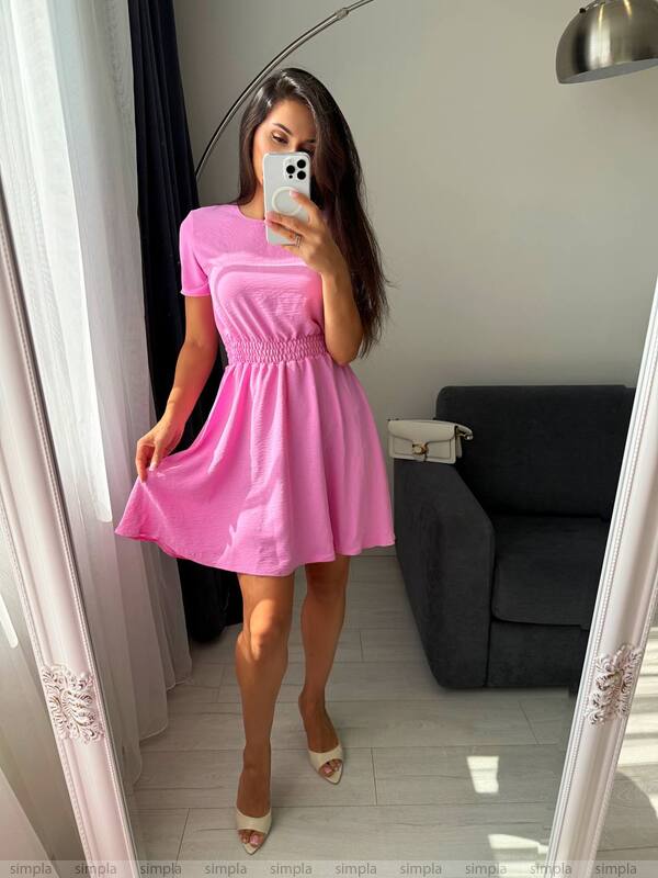 Woman in a pink dress taking a mirror selfie in a room with a gray sofa.