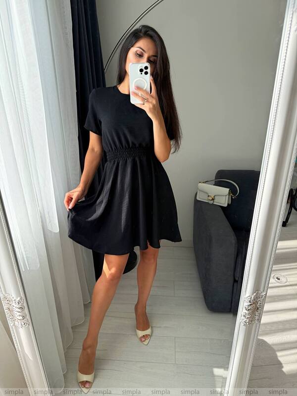 Woman taking a mirror selfie wearing a black dress in a room.