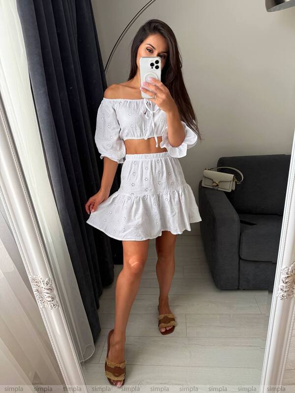 Woman taking a mirror selfie wearing a white off-shoulder top and skirt.
