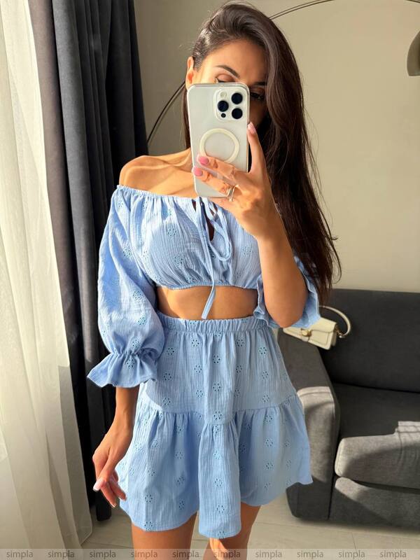 Woman wearing a light blue off-shoulder top and shorts, taking a mirror selfie.